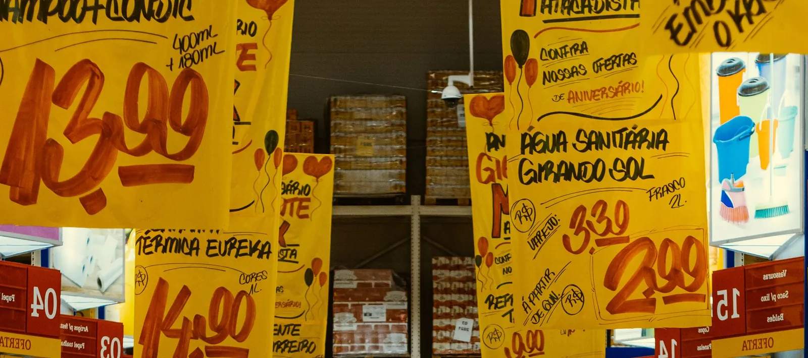 Corredor de supermercado com dezenas de cartazes amarelos de oferta pendurados, cada um escrito à mão com o preço.